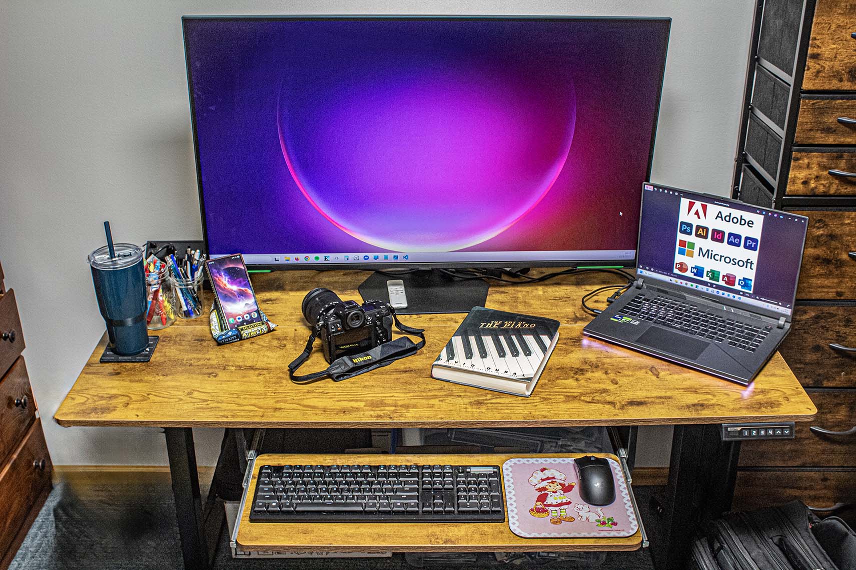 Home workspace with monitor, laptop, and Nikon camera on a wooden desk