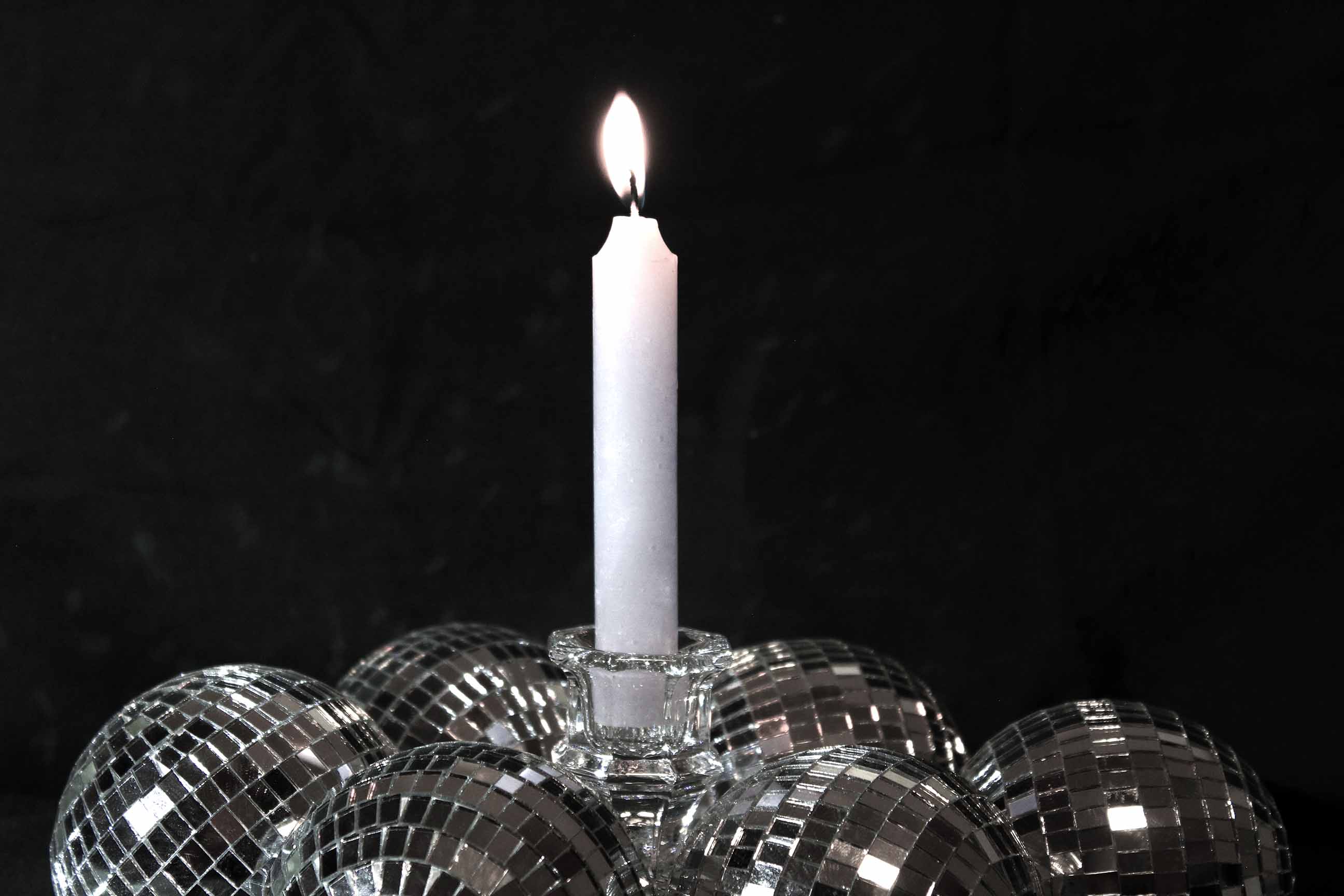 Single white candle burning in darkness, surrounded by mirrored glass spheres that reflect its light